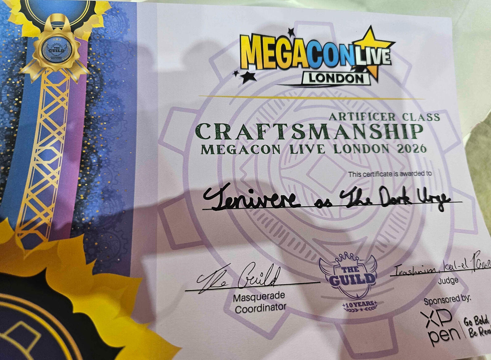 A certificate from MegaConLive London showing Artificer Class Craftsmanship award for Megacon Live London 2026 awarded to Jenivere as The Dark Urge, signed by the Masquerade Co-ordinators and the Judge